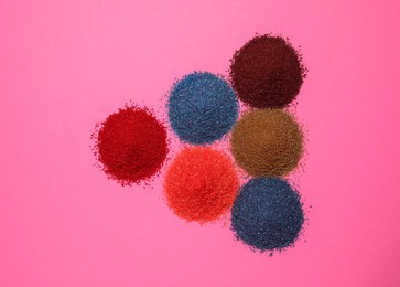 Photo of Heaps of different bright food coloring on pink background, flat lay