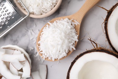 Photo of Coconut flakes, nut, grater and spoon on white marble table, flat lay