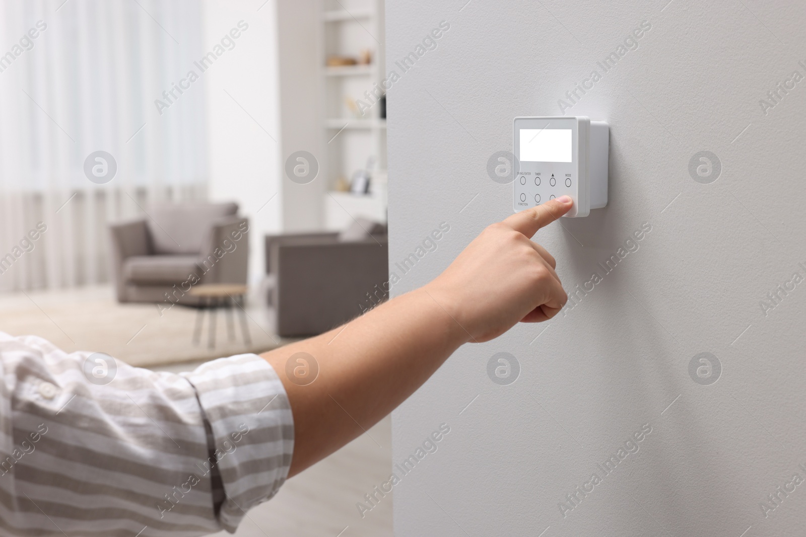 Photo of Man adjusting thermostat on white wall indoors, closeup. Smart home system