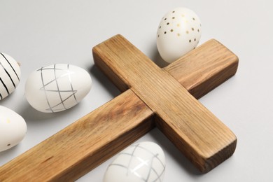 Photo of Wooden cross and painted Easter eggs on light grey background, closeup