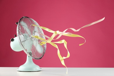 Photo of Electric fan on white table against pink background. Summer heat