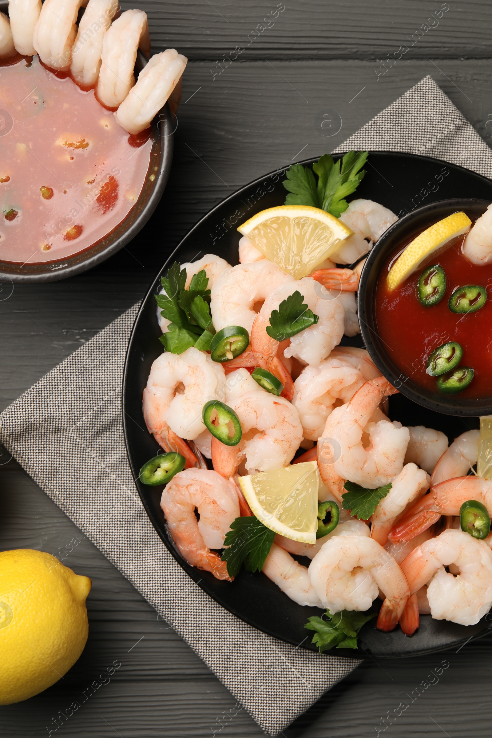 Photo of Tasty boiled shrimps with cocktail sauce, chili, parsley and lemon on grey wooden table, flat lay