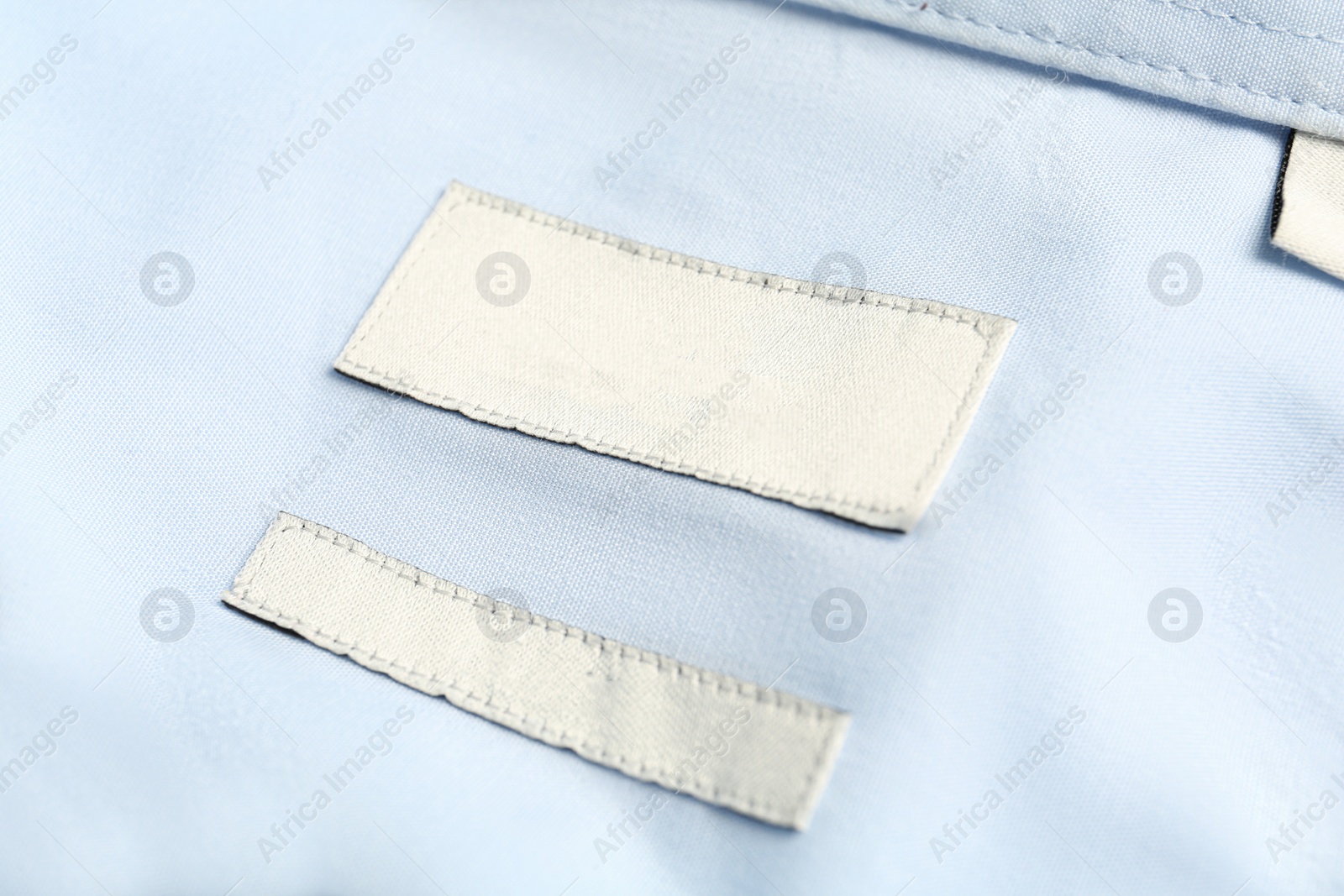 Photo of Blank clothing labels on light blue shirt, closeup