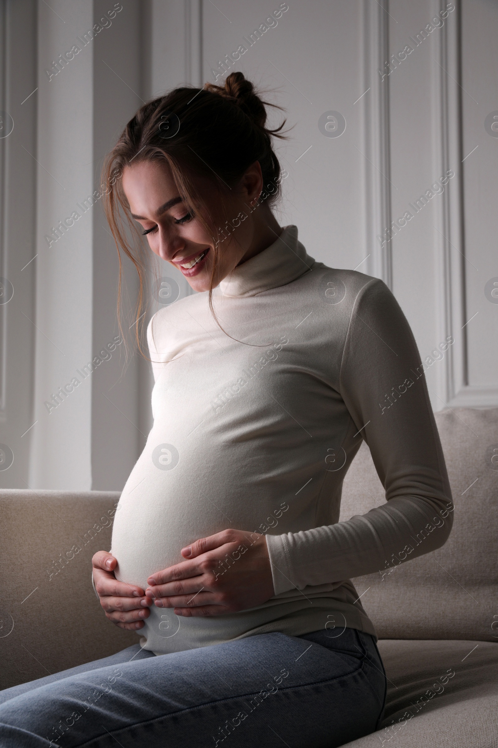 Photo of Young pregnant woman sitting on sofa at home