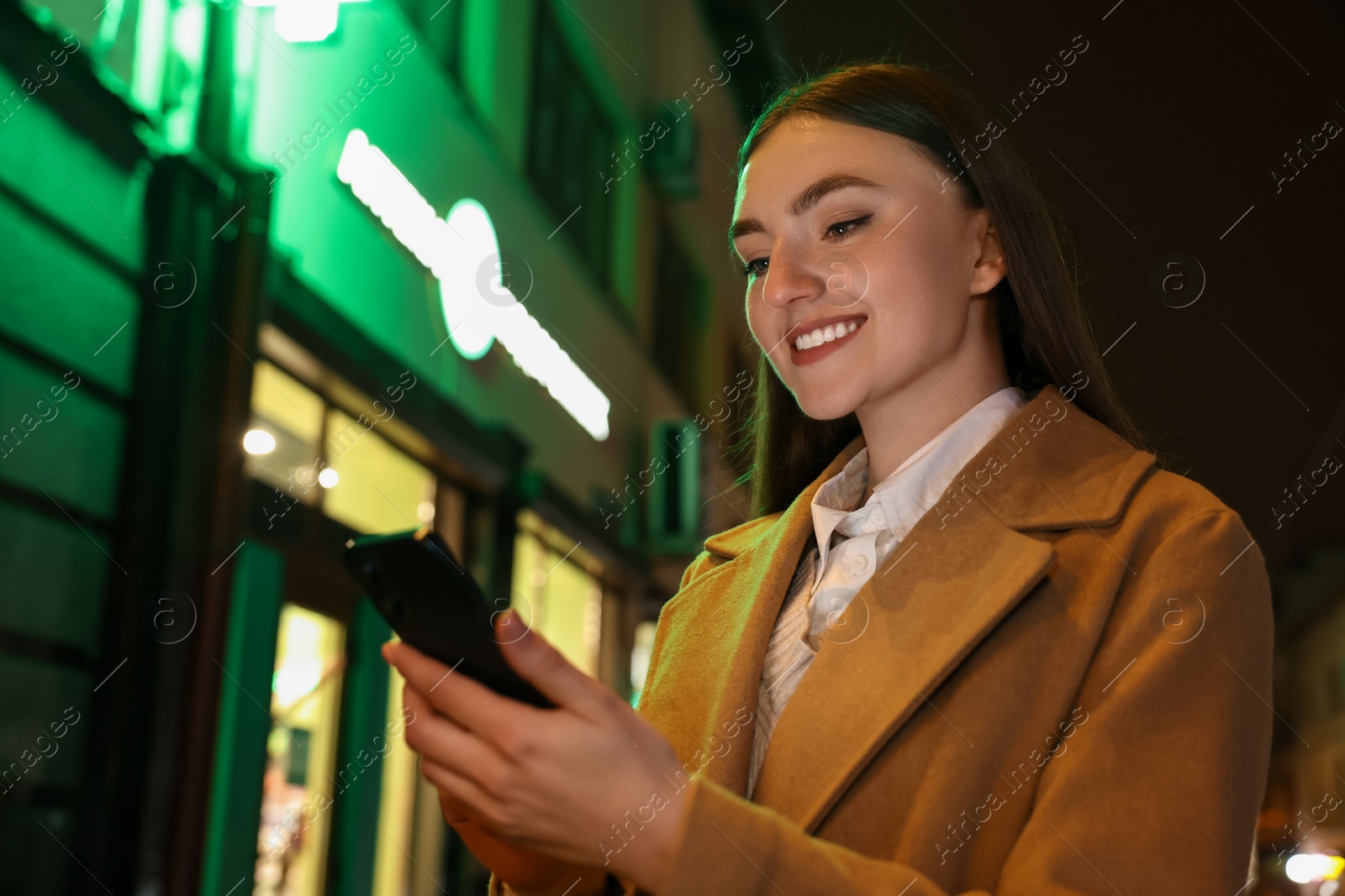 Photo of Smiling woman using smartphone on night city street. Space for text