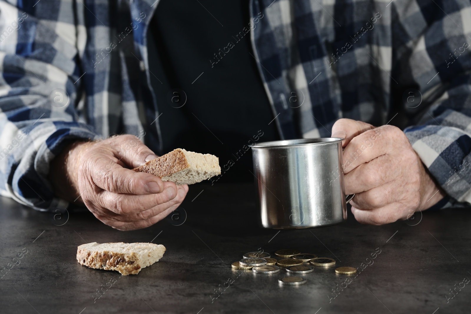 Photo of Poor elderly man with piece of bread and metal mug at table, closeup