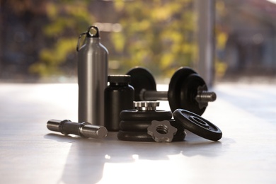 Photo of Adjustable dumbbells with bottle and jar of protein on floor indoors