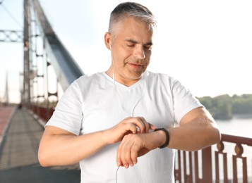 Photo of Handsome mature man looking at fitness tracker on bridge. Healthy lifestyle