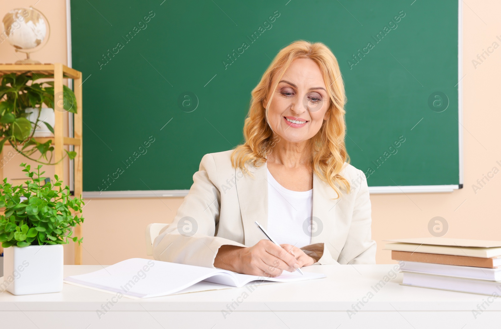 Photo of Professor giving lecture near green board at desk in classroom