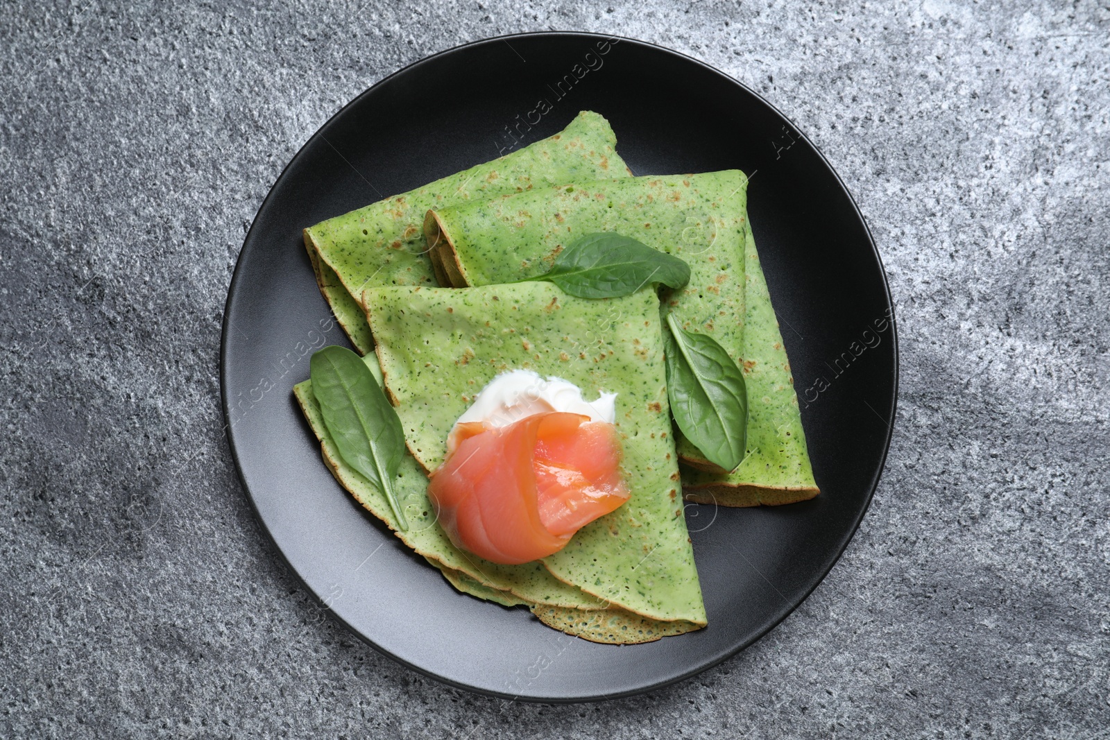 Photo of Delicious spinach crepes with salmon and cream on grey table, top view