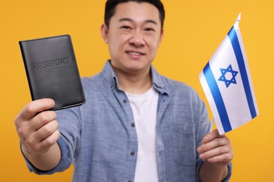 Photo of Immigration. Happy man with passport and flag of Israel on orange background, selective focus