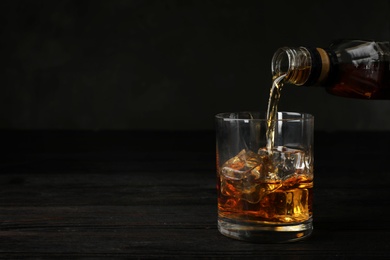 Pouring whiskey from bottle into glass with ice cubes on table. Space for text