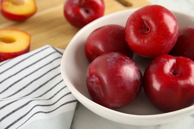 Delicious ripe plums in bowl on white table
