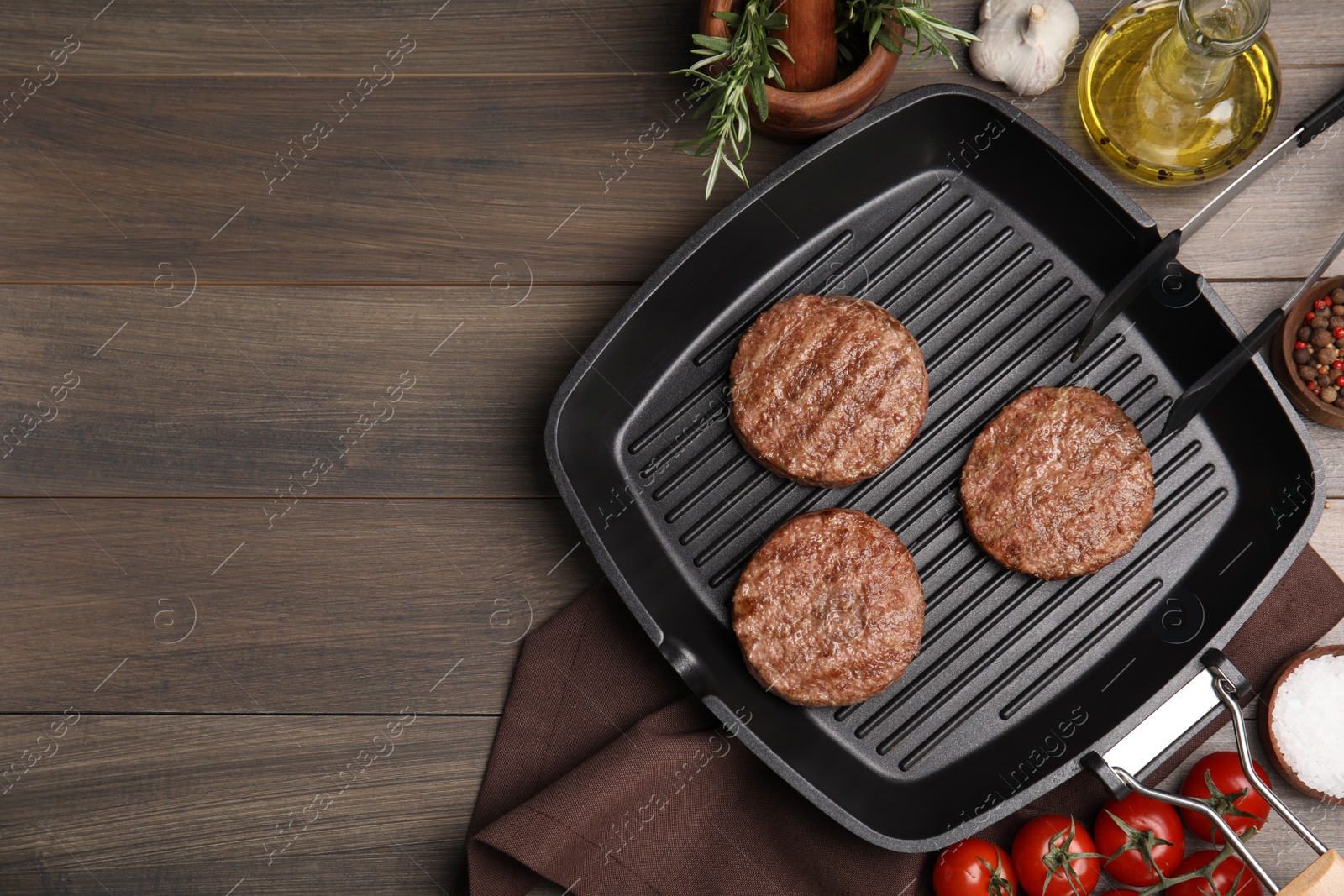 Photo of Grill pan with tasty fried hamburger patties and seasonings on wooden table, flat lay. Space for text