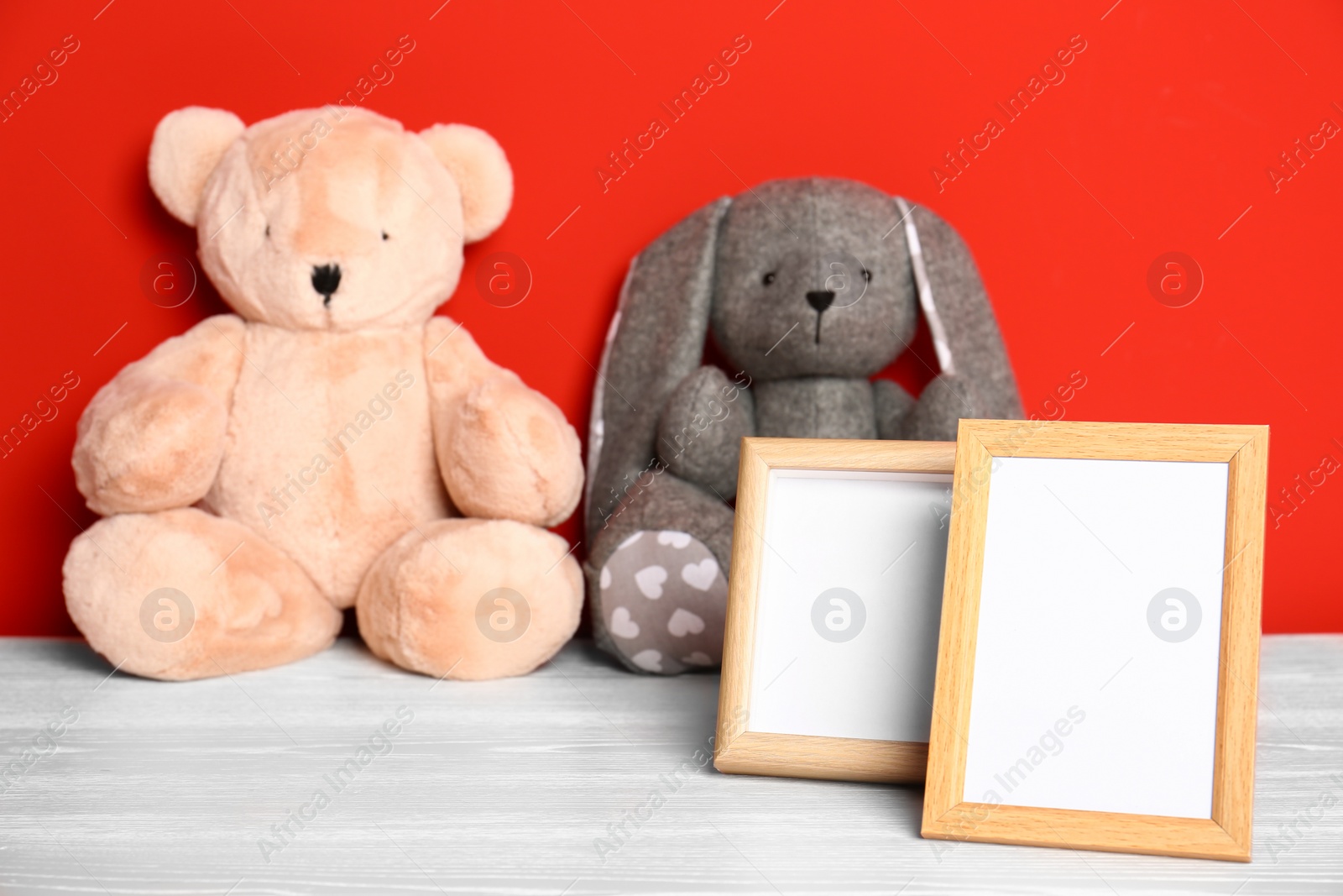 Photo of Soft toys and photo frames on table against red background, space for text. Child room interior