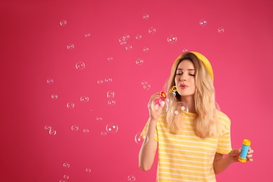 Young woman blowing soap bubbles on pink background, space for text