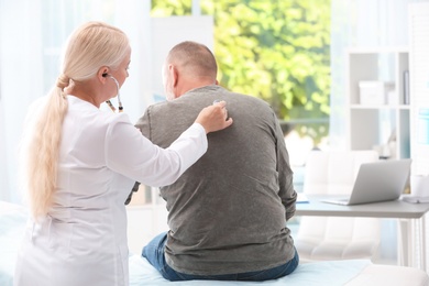 Doctor examining coughing mature man at clinic