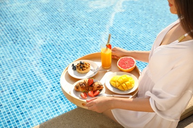 Young woman with delicious breakfast on tray near swimming pool, closeup