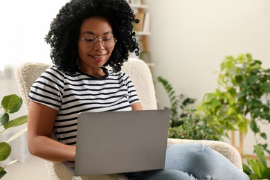 Relaxing atmosphere. Happy woman with laptop sitting on armchair near houseplants at home