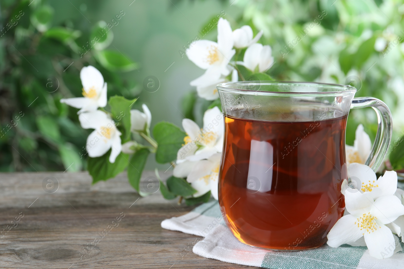 Photo of Cup of tea and fresh jasmine flowers on wooden table. Space for text