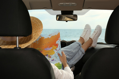 Young woman with world map in car, back view. Road trip