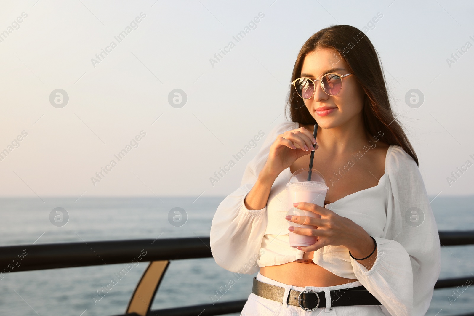 Photo of Beautiful woman with tasty milk shake near sea, space for text