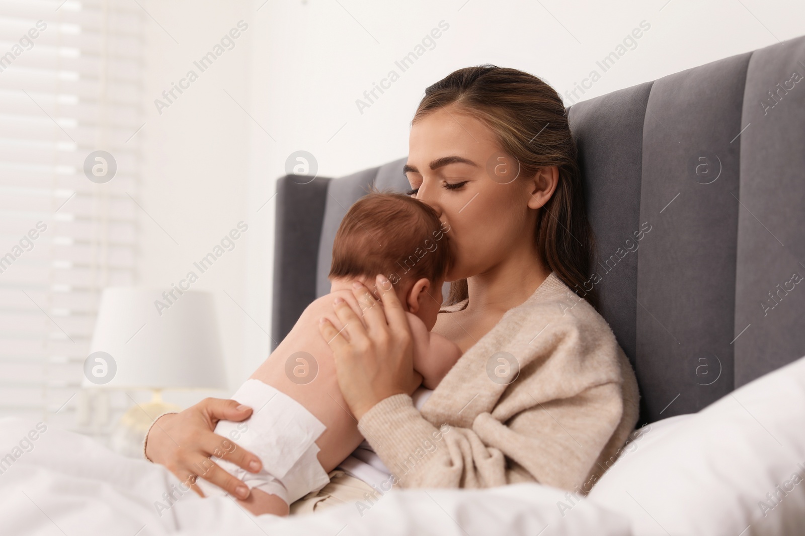 Photo of Mother kissing her cute newborn baby in bed indoors, space for text