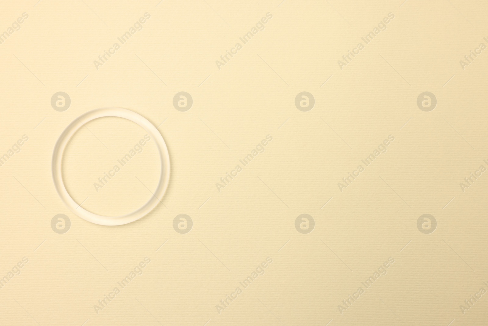 Photo of Diaphragm vaginal contraceptive ring on light yellow background, top view. Space for text