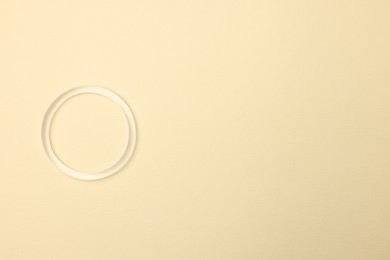 Photo of Diaphragm vaginal contraceptive ring on light yellow background, top view. Space for text