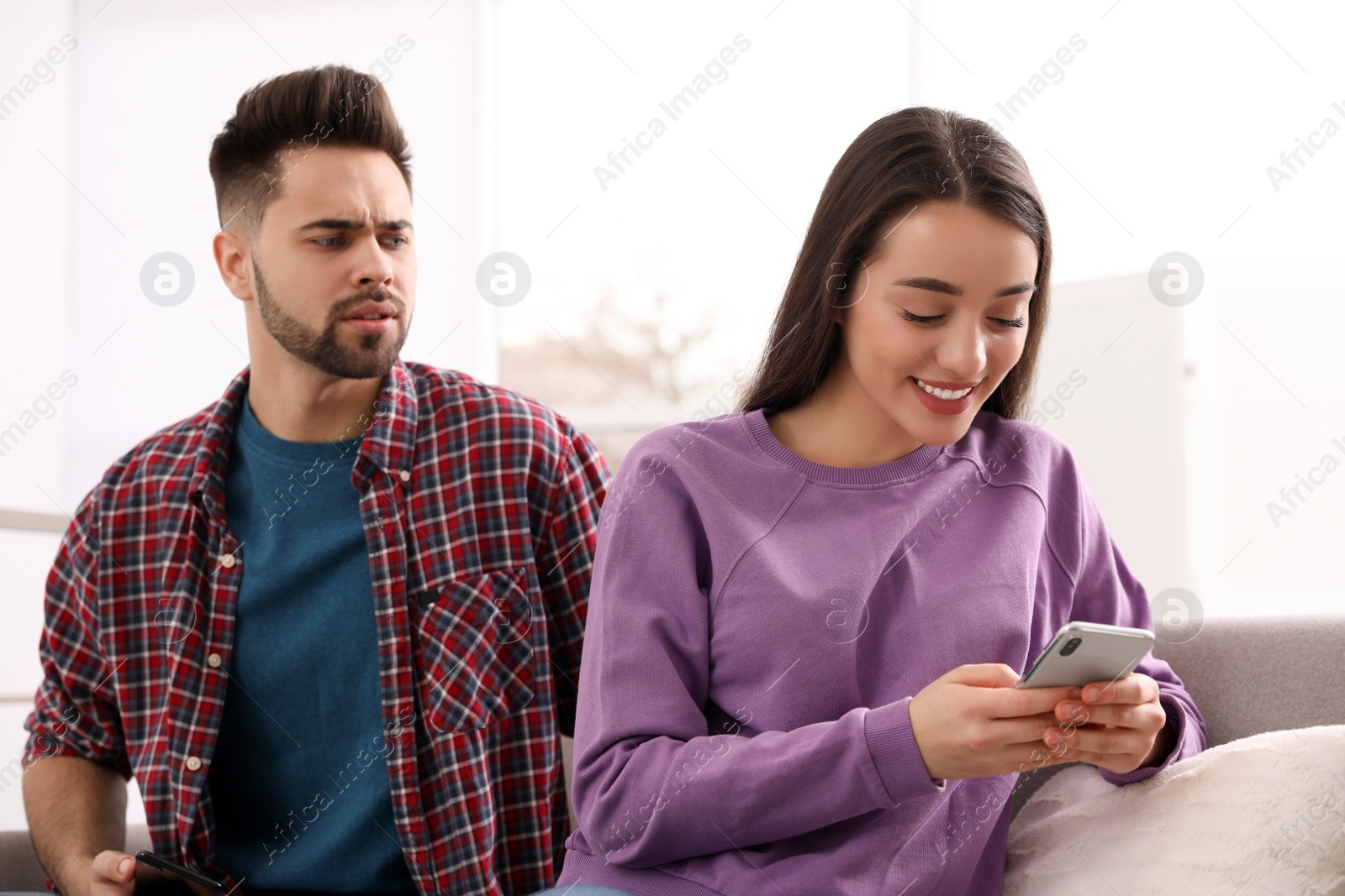 Photo of Distrustful young man peering into girlfriend's smartphone at home