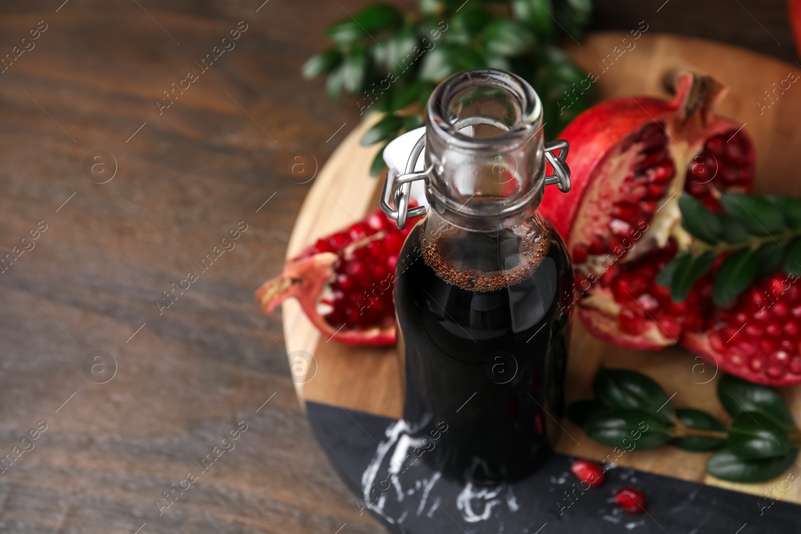 Photo of Tasty pomegranate sauce in bottle, fruits and branches on wooden table, closeup. Space for text