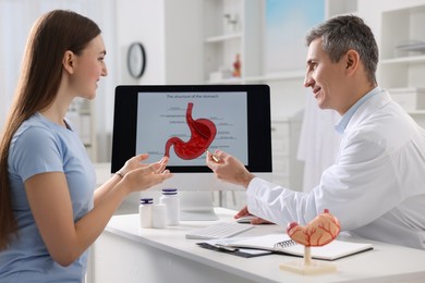 Gastroenterologist showing screen with illustration of human stomach model to patient at table in clinic