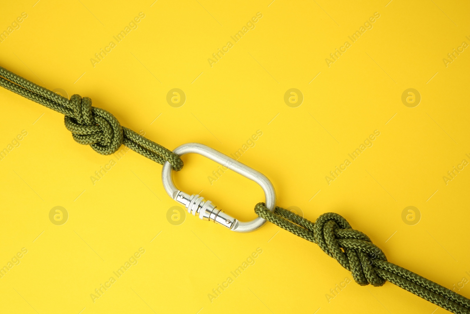 Photo of One metal carabiner with ropes on yellow background, top view