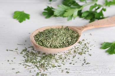 Photo of Spoon with dry parsley on white wooden table