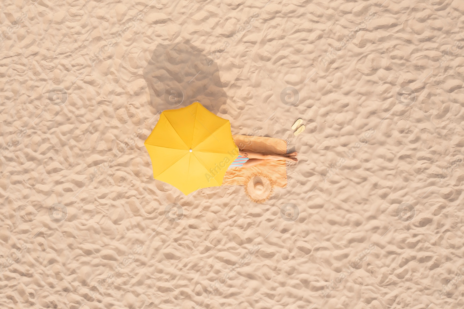 Image of Woman resting under yellow beach umbrella at sandy coast, aerial view