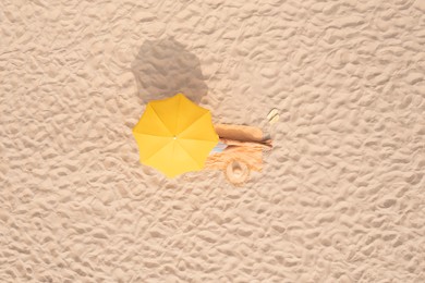 Woman resting under yellow beach umbrella at sandy coast, aerial view