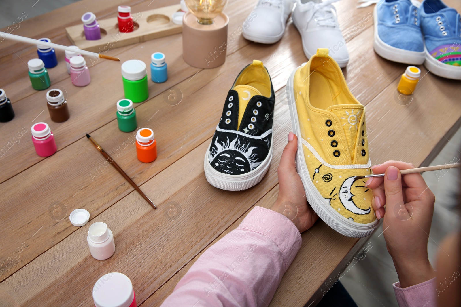 Photo of Woman painting on sneaker at wooden table, closeup. Customized shoes