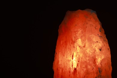 Photo of Himalayan salt lamp on dark background, closeup. Space for text