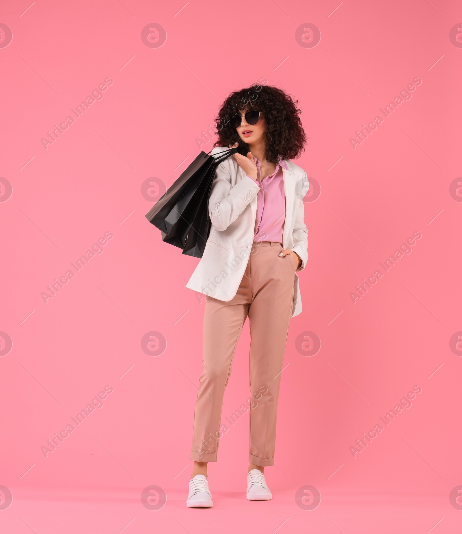 Photo of Happy young woman with shopping bags and stylish sunglasses on pink background. Space for text