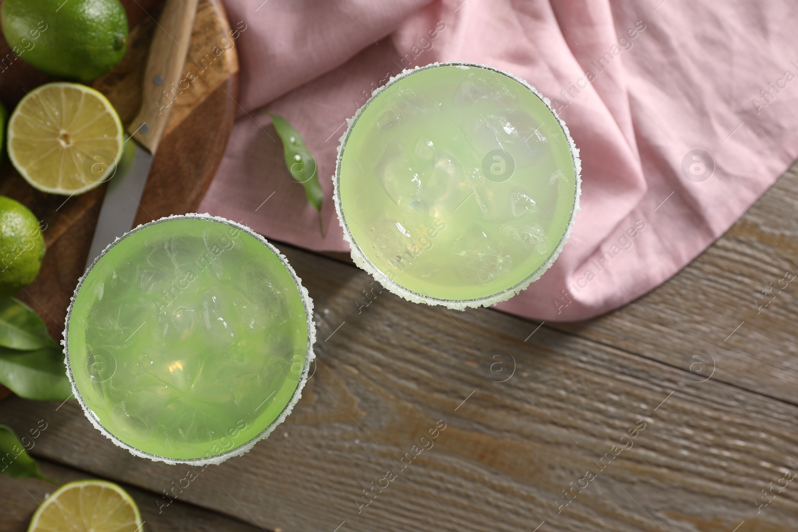 Photo of Delicious Margarita cocktail in glasses and lime on wooden table, flat lay. Space for text