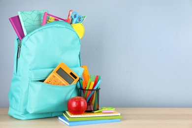 Bright backpack with school stationery on brown wooden table against light background, space for text
