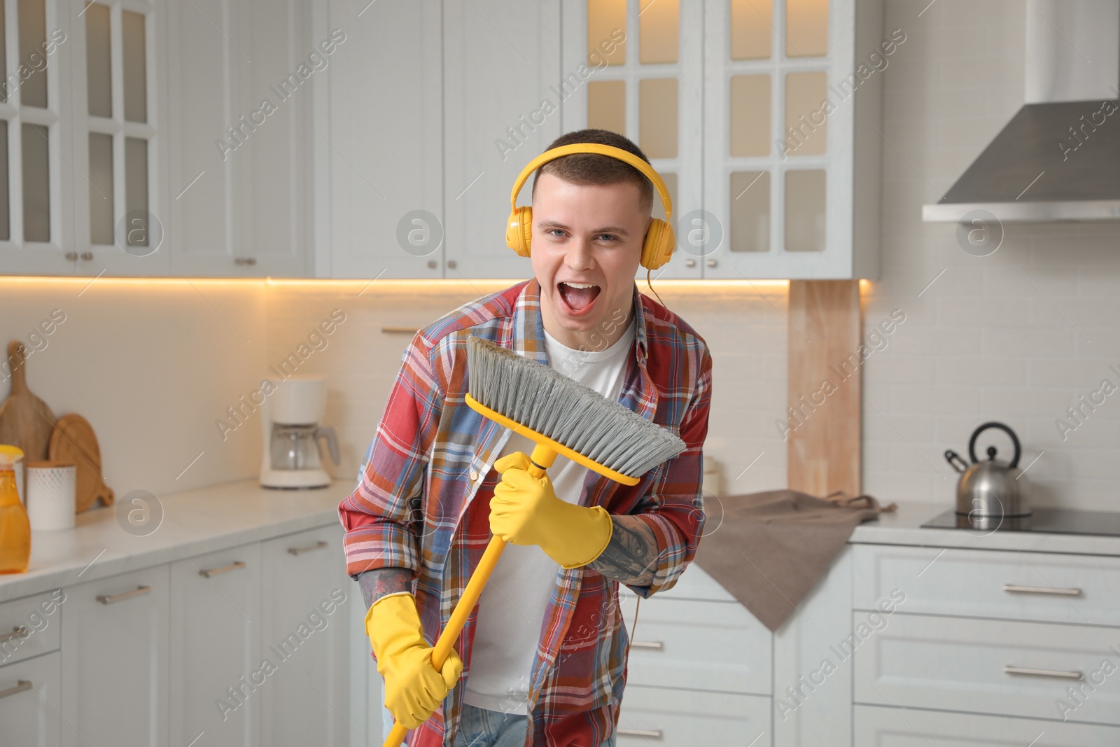 Photo of Handsome young man with headphones singing while cleaning kitchen