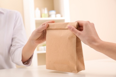 Woman giving paper bag with order to customer in shop, closeup. Mock up for design