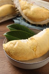 Photo of Bowl with piecefresh ripe durian and leaves on wooden table, closeup