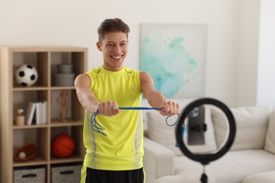 Photo of Smiling sports blogger holding skipping rope while streaming online fitness lesson with smartphone at home