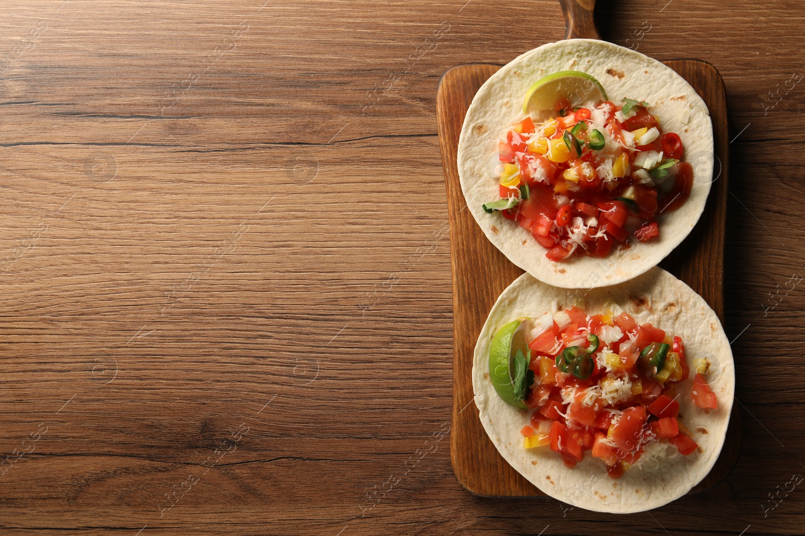 Photo of Delicious tacos with vegetables, lime and ketchup on wooden table, top view. Space for text