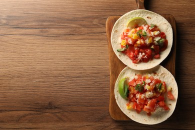 Photo of Delicious tacos with vegetables, lime and ketchup on wooden table, top view. Space for text