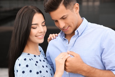 Photo of Lovely couple looking at beautiful engagement ring outdoors