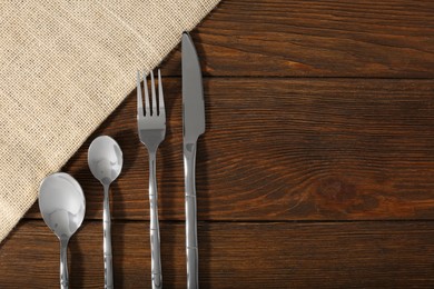 Stylish cutlery set and napkin on wooden table, flat lay. Space for text