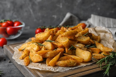 Photo of Wooden board with baked potatoes and rosemary on table